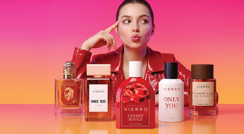A woman posing alongside a collection of Vierro women's perfume bottles against a warm, pink-toned background.